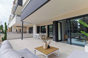 An outdoor patio with a sofa, a wooden table with a vase, and a cactus plant. - Groundfloor Villamartin Amanecer (Orihuela)