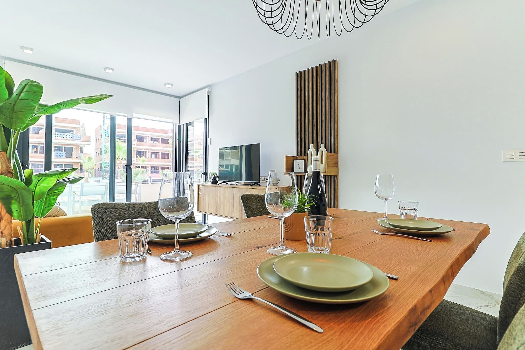 A dining table set with plates, glasses, and cutlery, a potted plant, and a modern light fixture.