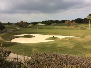 Ein Golfplatz mit Sandbunkern, einem gewundenen Weg und Bäumen sowie einem bewölkten Himmel im Hintergrund.