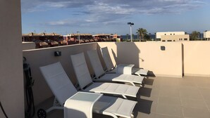 A rooftop terrace with white lounge chairs and a view of the sea and buildings in the background. - Penthouse Higuericas Playas (Pilar de la Horadada)