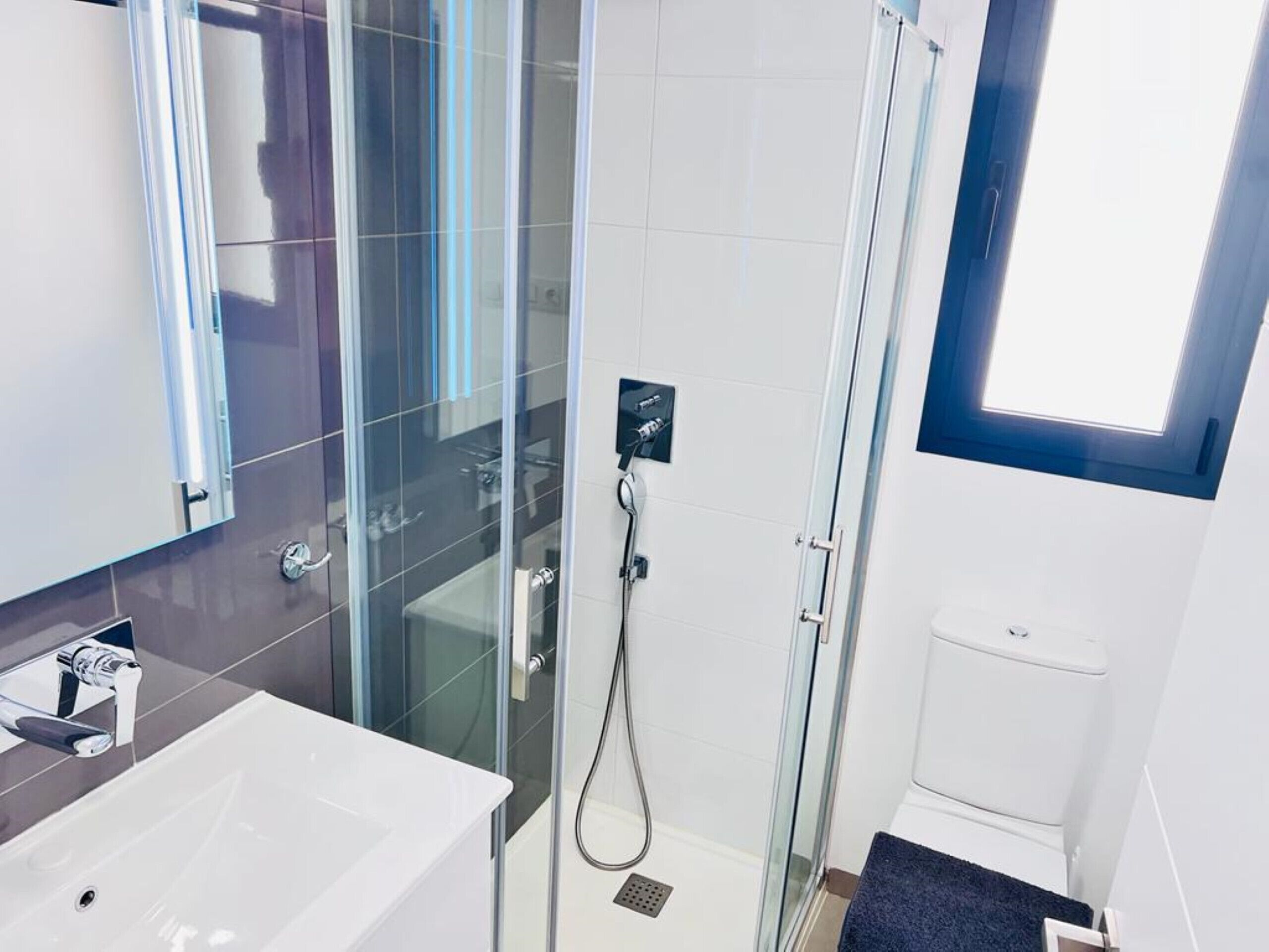 Ein modernes Badezimmer mit einer Duschkabine, einem weißen Waschbecken und einer Toilette.