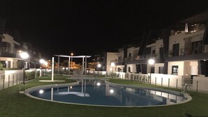A nighttime view of a swimming pool surrounded by modern buildings with balconies. - Penthouse Higuericas Playas (Pilar de la Horadada)