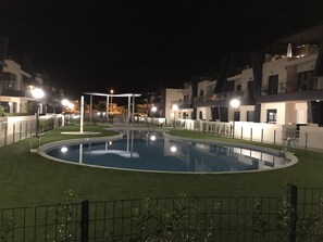 Ein Nachtblick auf einen Swimmingpool, umgeben von modernen Gebäuden mit Balkonen.