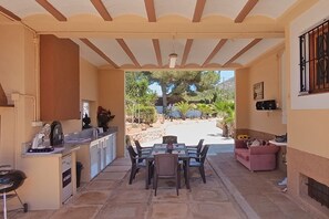 Eine Terrasse im Freien mit Esstisch und Stühlen, einer kleinen Küche und einer Sitzecke mit einer Couch.