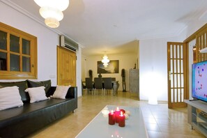 Ein Wohnzimmer mit einer Couch, einem Couchtisch mit Kerzen, einem Fernseher und einem Essbereich im Hintergrund.