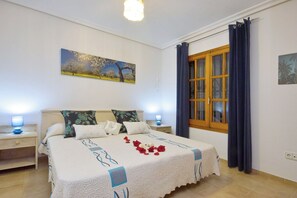 Ein Schlafzimmer mit einem großen Bett, zwei Nachttischen, einem Fenster mit Vorhängen und einem Bild an der Wand.