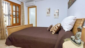 Quarto com uma cama grande, janela com cortinas, ar condicionado fixado na parede e uma estátua decorativa de Buda.