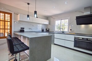 A modern kitchen with a marble backsplash, stainless steel appliances, and a bar area with stools. - Villa Ruly (IB)