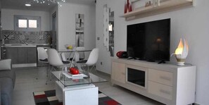 Ein modernes Wohnzimmer mit einem Glastisch, einem Flachbildfernseher und einem Kamin.