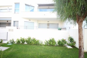 A modern two-story building with a white facade, a balcony on the upper floor, and a small garden area with grass and shrubs. - Groundfloor Property Amalia Torrevieja (Torrevieja)