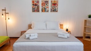 Ein ordentlich bezogenes Bett mit weißen Leinen, zwei Nachttische mit Lampen und drei Blumenbilder an der Wand.