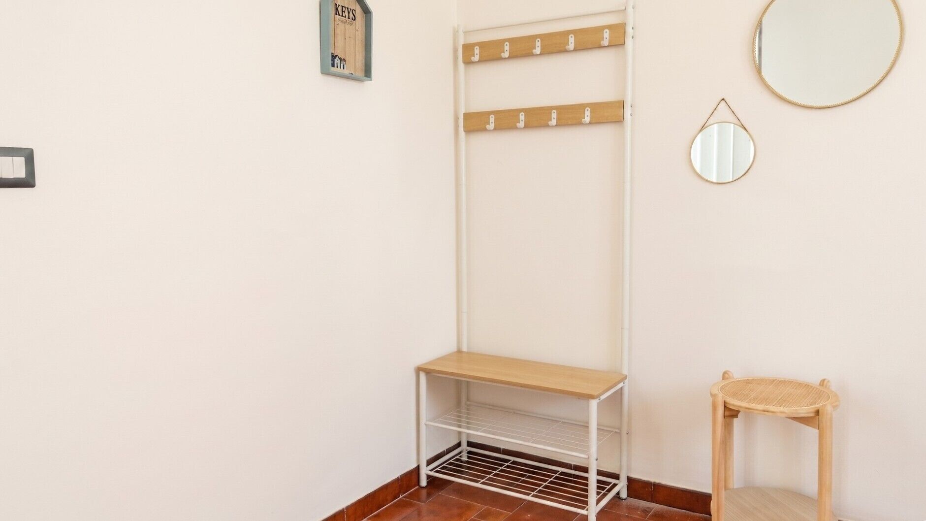 Een hoek van een kamer met een kapstok, een kleine tafel, een spiegel en een lichtschakelaar op de muur.