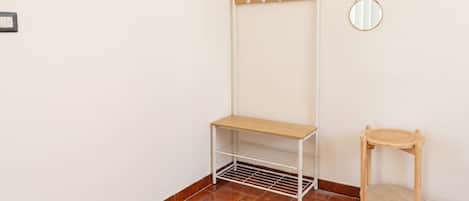 A corner of a room with a coat rack, a small table, a mirror, and a wall-mounted light switch.