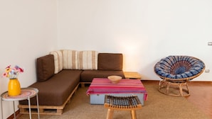 A cozy living area with a brown sofa, a colorful striped table, a wicker chair, and a small wooden stool. - Chez Mich - Two Bedroom Apartment, Sleeps 5 (Alghero)