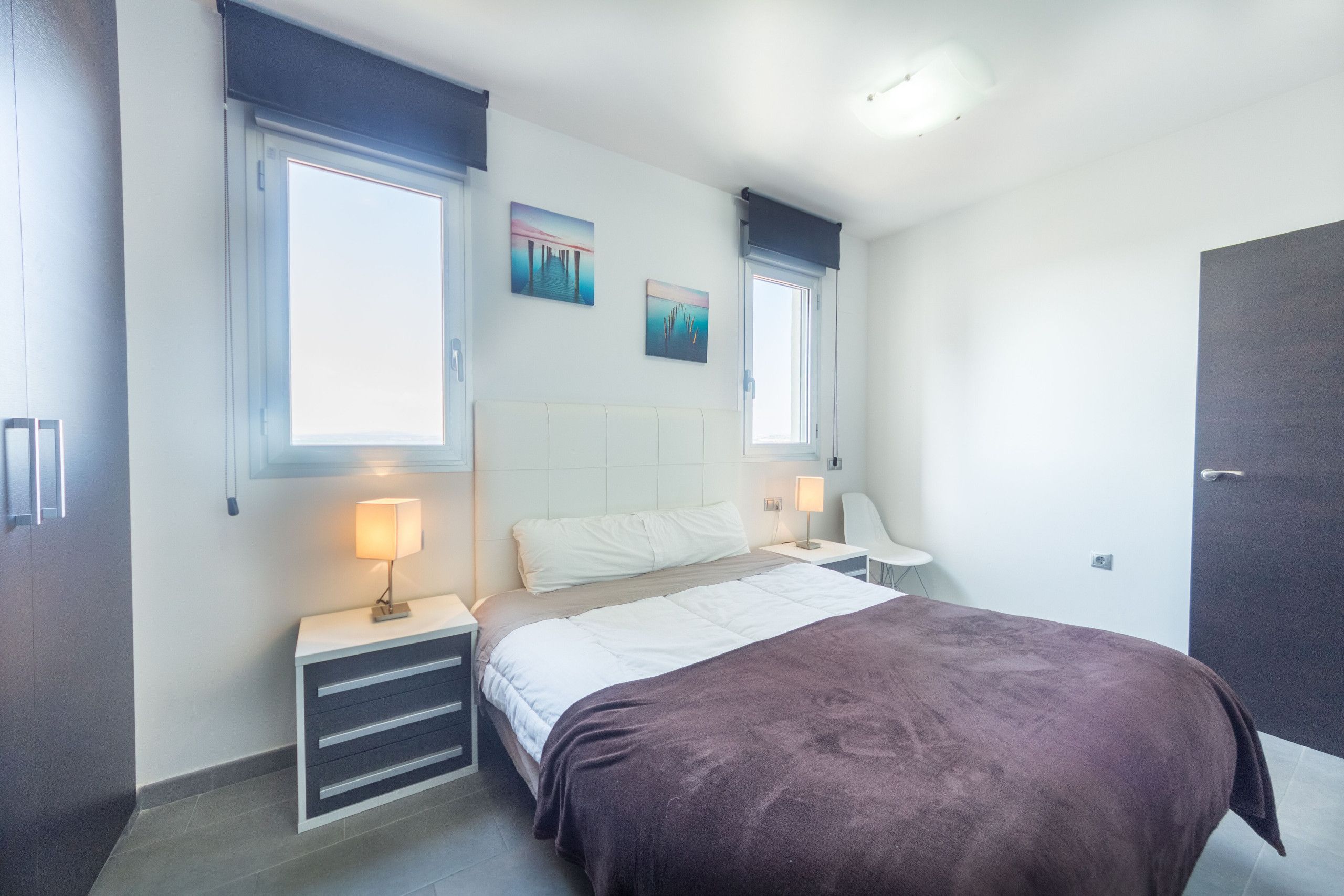 A bedroom with a bed, bedside tables, a nightstand, a window with curtains, and a door.