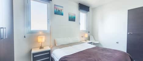 A bedroom with a bed, bedside tables, a nightstand, a window with curtains, and a door.
