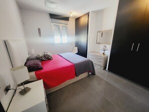 Een moderne slaapkamer met een bed, nachtkastje, lamp, kledingkast en een raam met jaloezieën.