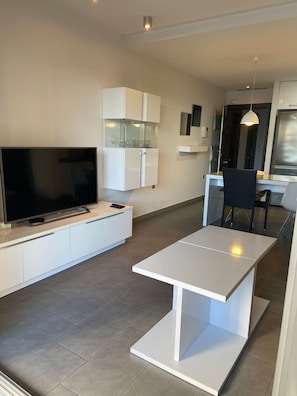 Een moderne keuken met een flatscreen televisie, witte kasten en een eethoek met een tafel en stoelen.