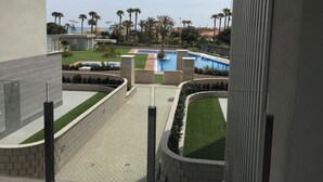A view of a swimming pool area with multiple pools, surrounded by palm trees and greenery, with a clear sky above. - Apartment Aqua Nature La Mata (Torrevieja)