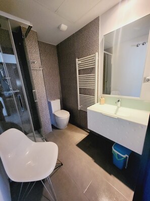 A modern bathroom with a glass shower enclosure, a white toilet, a towel rack, and a large mirror above the sink. - Apartment Aqua Nature La Mata (Torrevieja)