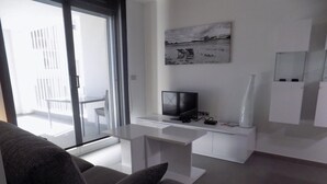 A modern living room with a grey sofa, a white desk with a TV, and a painting on the wall. - Apartment Aqua Nature La Mata (Torrevieja)
