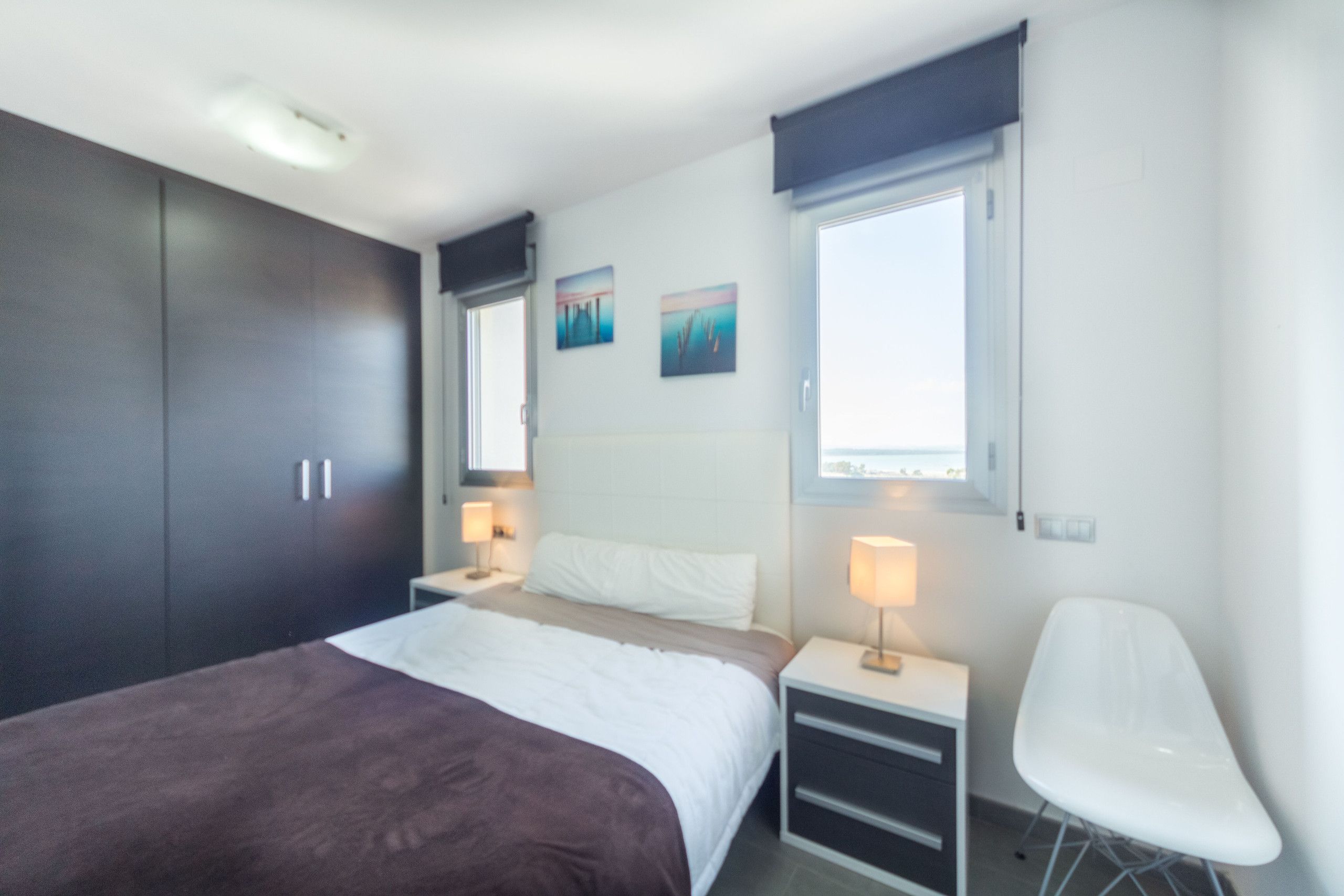 A modern bedroom with a bed, bedside tables, a chair, and artwork on the wall.