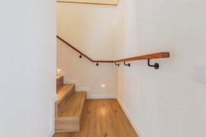 Un escalier avec des marches en bois et une rampe, un interrupteur sur le mur et un petit spot encastré dans le sol.