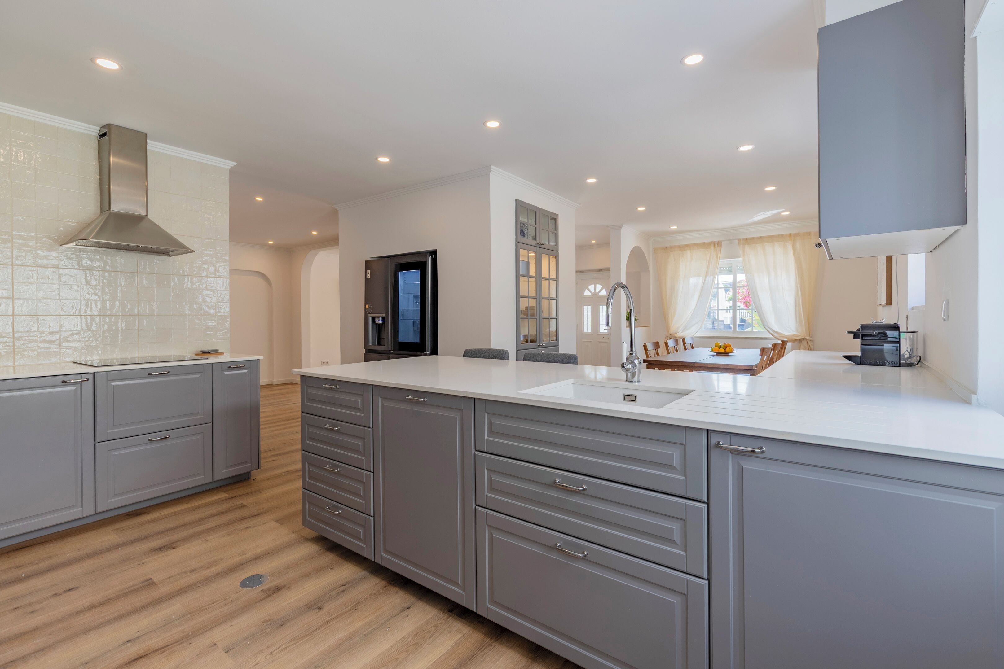 A modern kitchen with grey cabinetry, a large island, and a built-in oven.