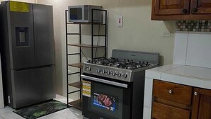 A kitchen with a stainless steel refrigerator, a microwave on a shelf, a gas stove, and a tiled backsplash. - Havendale Suite Retreat (Kingston)