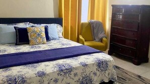A bedroom with a bed, a chair, a dresser, and a painting on the wall. - Havendale Suite Retreat (Kingston)