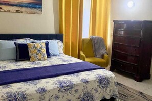 Ein Schlafzimmer mit einem Bett, einem Sessel, einer Kommode und einem Bild an der Wand.