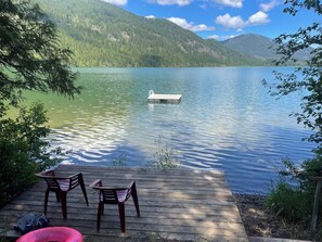 Eine Holzsteg mit Stühlen, ein Ponton und ein See mit Bergen im Hintergrund.