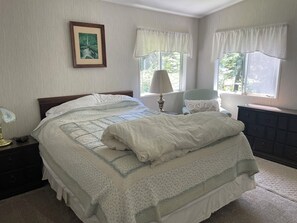 Ein ordentlich bezogenes Bett mit einem blumigen Überwurf, einer Nachttischlampe und einem gerahmten Bild an der Wand.
