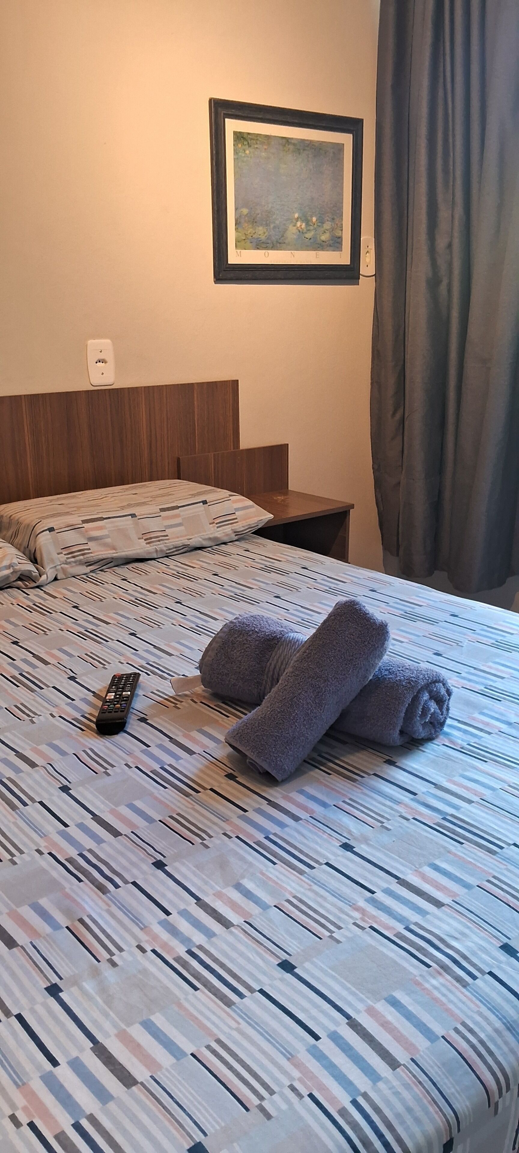 A hotel room with a bed, a remote control, and a framed picture on the wall.