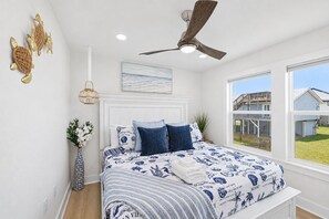 A bedroom with a bed, a ceiling fan, a window, and a view of a house. - Beachfront, Hot Tub, Arcade, Foosball, Steps to beach, outdoor games & MORE (Galveston)