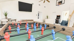 Een tafelvoetbaltafel in een woonkamer met een aan de muur bevestigde televisie en een basketbalring.