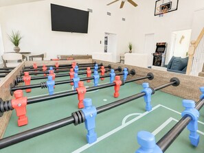 A foosball table in a living room with a TV mounted on the wall and a basketball hoop. - Beachfront, Hot Tub, Arcade, Foosball, Steps to beach, outdoor games & MORE (Galveston)