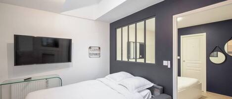 A bedroom with a bed, a TV, a radiator, and a door leading to another room.