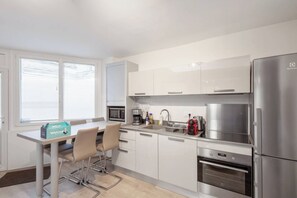 Eine moderne Küche mit weißen Schränken, Edelstahlgeräten, einer Kaffeemaschine und einem Toaster. Es gibt einen Tisch mit Stühlen und eine Willkommensbox.