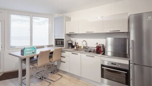 Eine moderne Küche mit weißen Schränken, Edelstahlgeräten, einer Kaffeemaschine und einem Toaster. Es gibt einen Tisch mit Stühlen und eine Willkommensbox.