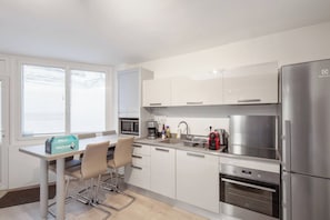 A modern kitchen with white cabinets, stainless steel appliances, a coffee maker, and a toaster. There is a table with chairs and a welcome box. - Beautiful Modern Apartment for 4 near Bastille (Paris)