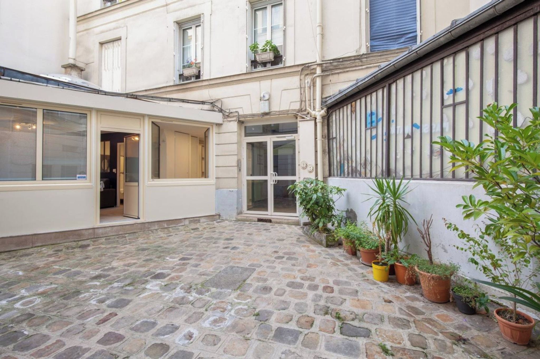 A courtyard with a stone floor, a glass door entrance, and potted plants along the wall.