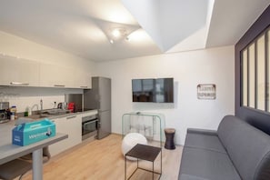 A modern kitchen with a built-in oven and a dining area with a grey sofa and a small table. - Beautiful Modern Apartment for 4 near Bastille (Paris)