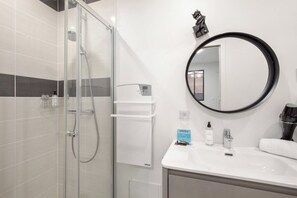 Ein modernes Badezimmer mit Duschkabine aus Glas, einem runden Spiegel und einem weißen Waschtisch.
