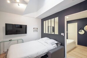 Ein Schlafzimmer mit einem Bett, einem Fernseher, einem Heizkörper und einer Tür zu einem anderen Raum.