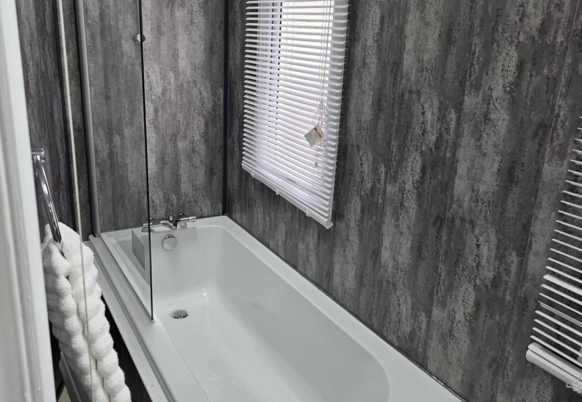 A bathroom with a bathtub, a towel rack, and a window with blinds.