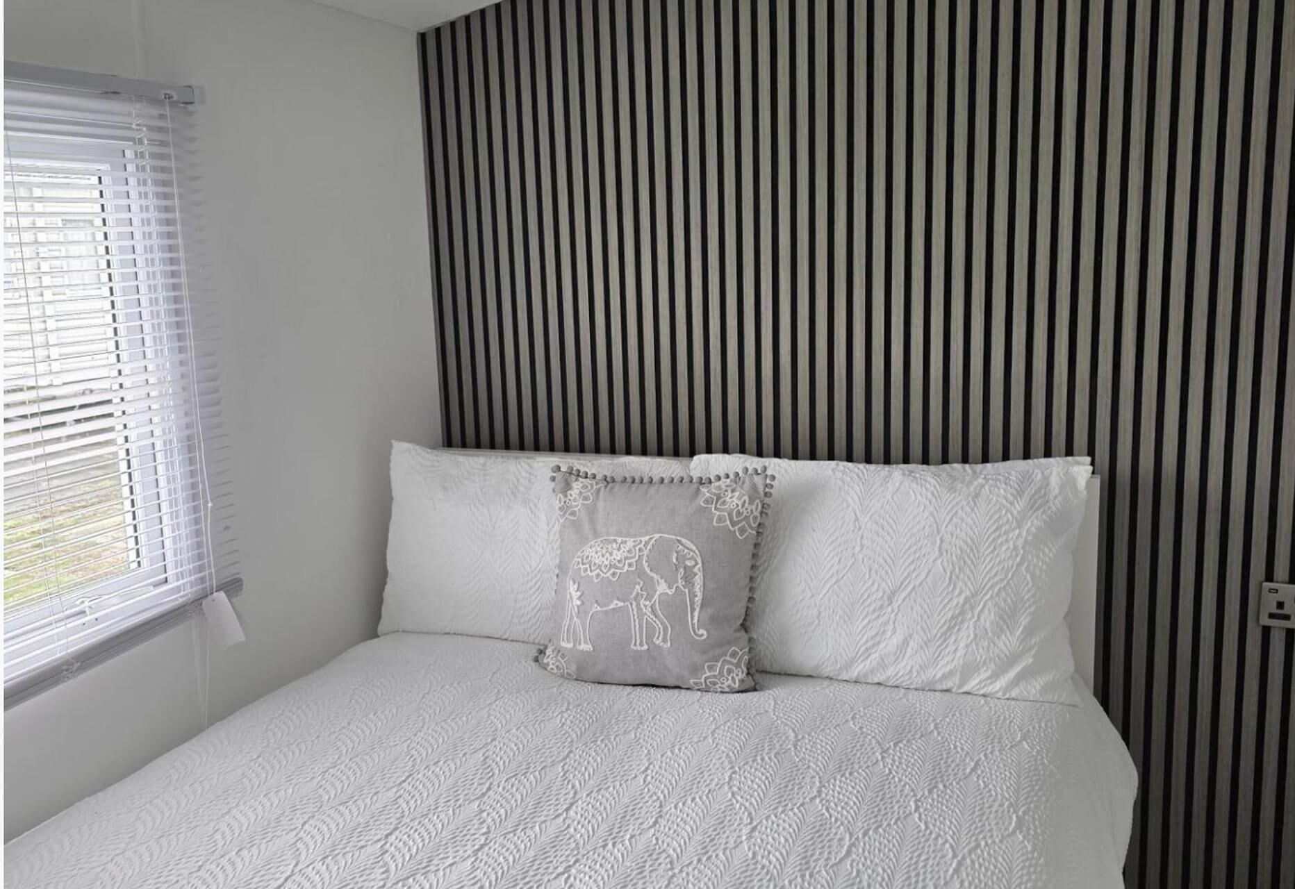 A bedroom with a bed, a window with blinds, and a striped wall.