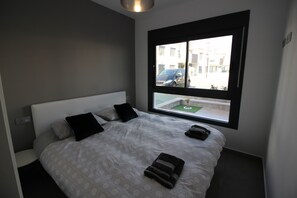 Una habitación de hotel moderna con una cama grande, un ventanal con vista a la calle y un balcón pequeño.