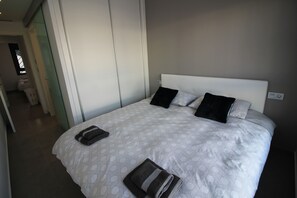Ein ordentlich bezogenes Bett mit einer gemusterten Tagesdecke, zwei Kissen und einem gefalteten Handtuch daneben.
