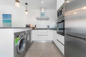 Eine moderne Küche mit integriertem Waschmaschine, Edelstahlgeräten und Pendelleuchten.